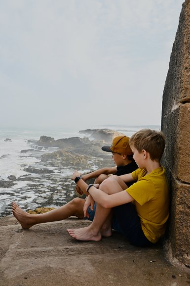 Kinder sitzen nebeneinander und schauen auf das Meer – Marokko mit Kindern