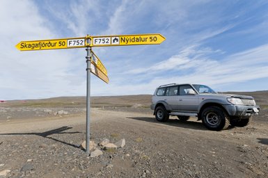 Ein silberner Geländewagen steht an einem Wegweiser, der in die Richtungen Skagafjörður und Nýidalur zeigt.