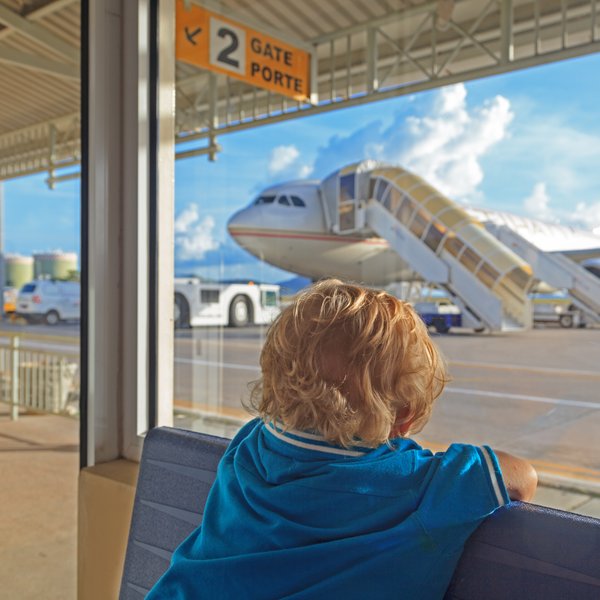Ein kleines Kind mit blonden Locken sitzt am Fenster und beobachtet ein Flugzeug, das am Gate parkt.
