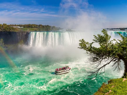 Die Niagarafälle stürzen majestätisch in den türkisfarbenen Fluss, während ein Boot mit Touristen in der Nähe fährt.