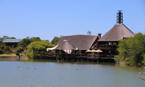 Ein malerisches Lodge-Gebäude mit Strohdach am Ufer eines ruhigen Sees, umgeben von üppigem Grün und klarem Himmel.
