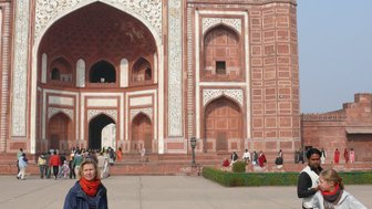 Eine Frau steht vor dem beeindruckenden Taj Mahal, während andere Besucher im Hintergrund die Architektur bewundern.