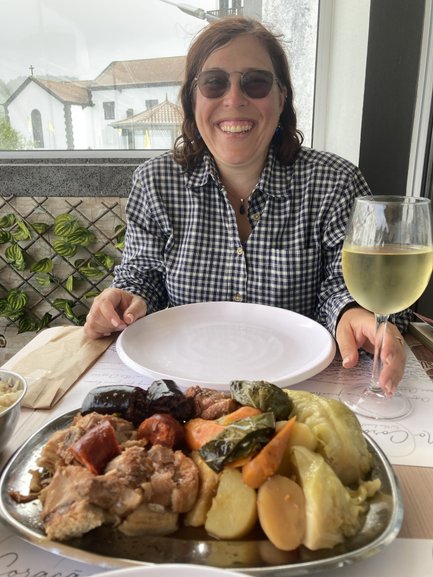 Eine fröhliche Frau mit Sonnenbrille lächelt, während sie ein köstliches Gericht mit Fleisch und Gemüse genießt.