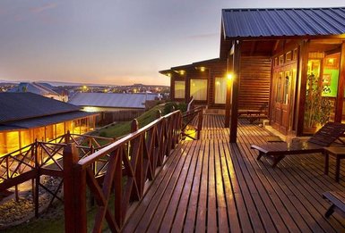 Eine Holzterrasse mit Blick auf ein Hotel, beleuchtet von warmem Licht, während die Dämmerung den Himmel färbt.