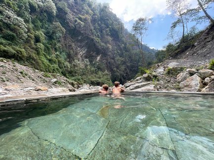 Zwei Personen entspannen in einem heißen Quellbecken, umgeben von einer beeindruckenden Berglandschaft in Nepal.