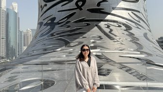 Eine Frau steht auf einer modernen Plattform mit reflektierender Oberfläche, umgeben von futuristischer Architektur und Wolkenkratzern.