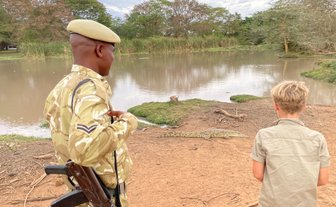 Ein Sicherheitsbeamter in Uniform beobachtet einen Jungen, der fasziniert auf einen Krokodil am Ufer schaut.