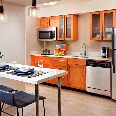 Eine moderne Küchenzeile mit Holzschränken, Edelstahlgeräten und einem kleinen Essbereich mit zwei Stühlen.