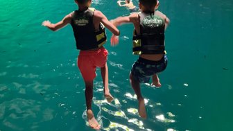 Zwei Jungen springen fröhlich ins klare Wasser eines Cenotes, während andere Schwimmer im Hintergrund zu sehen sind.