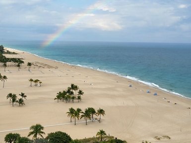 Ein Regenbogen spannt sich über den Himmel, während sanfte Wellen an den goldenen Strand von Fort Lauderdale schlagen.