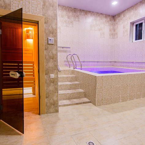 Ein eleganter Saunabereich mit einem gläsernen Eingang und einem kleinen Pool, der sanft beleuchtet ist.