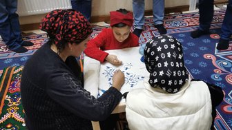 Drei Frauen und ein Mädchen sitzen auf einem bunten Teppich und arbeiten gemeinsam an traditioneller Stickerei.