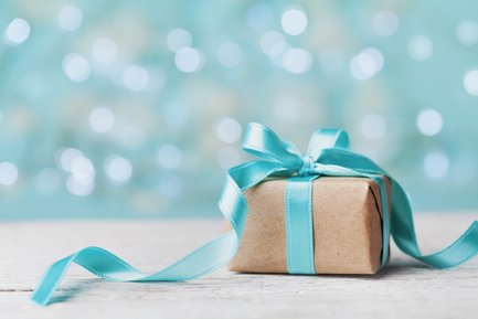 Ein hübsch verpacktes Geschenk in braunem Papier mit einer hellblauen Schleife, auf einem hellen Holztisch platziert.