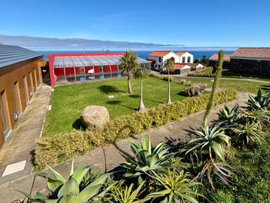 Ein gepflegter Garten mit grüner Rasenfläche, umgeben von modernen Gebäuden und Blick auf das Meer im Hintergrund.