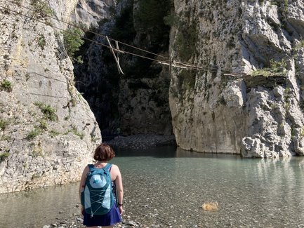 Eine Person steht am Ufer eines klaren Gewässers, umgeben von hohen, steilen Felsen und einer malerischen Landschaft.