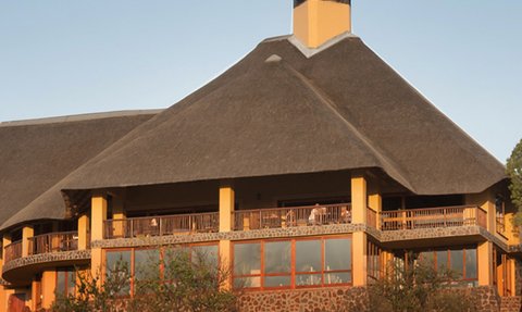 Ein großes, gelbes Lodge-Gebäude mit einem markanten Strohdach, umgeben von sanften Hügeln und Bäumen.