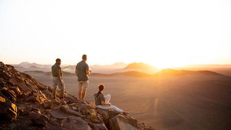 Drei Personen genießen den Sonnenuntergang in der Wüste - Namibia mit Kindern