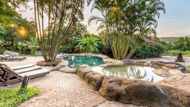 Ein einladender Außenbereich mit einem natürlichen Pool, umgeben von üppigem Grün und Palmen, ideal zum Entspannen.