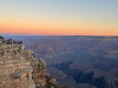 Eine Gruppe von Menschen steht am Rand des Grand Canyon und bewundert die atemberaubende Aussicht bei Sonnenuntergang.