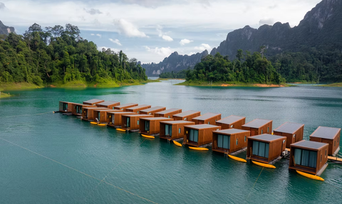 Eine Reihe von modernen, schwimmenden Bungalows liegt auf einem ruhigen, türkisfarbenen See, umgeben von üppiger Natur.