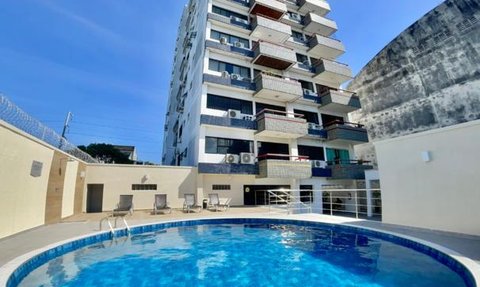 Ein blauer Pool reflektiert den klaren Himmel, umgeben von einem modernen Apartmentgebäude mit Balkonen.