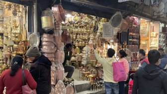 In einer belebten Straße in Kathmandu betrachten Menschen eine Vielzahl von Kupferwaren und Souvenirs in einem Geschäft.