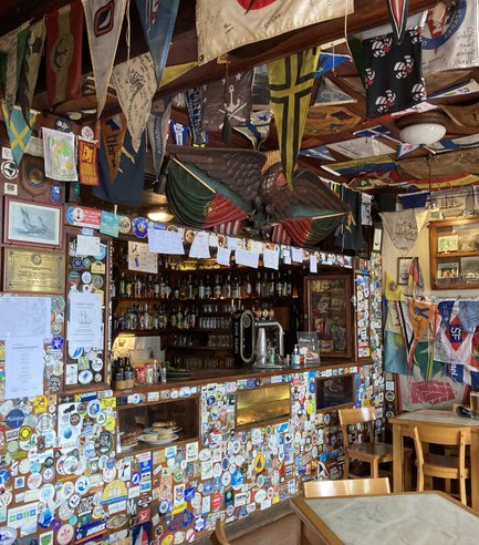Die Bar ist mit zahlreichen Aufklebern und Flaggen dekoriert, die eine maritime Atmosphäre schaffen und Geschichten erzählen.
