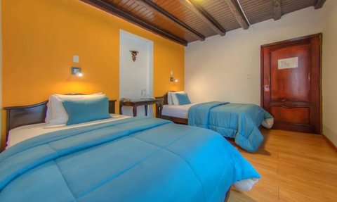 Zwei Betten mit blauen Bettdecken in einem hellen Zimmer mit orangefarbenen Wänden und Holzdecke.