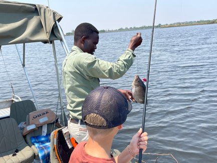 Ein Angler hält stolz einen gefangenen Fisch über dem Wasser, während ein Junge gespannt zuschaut.