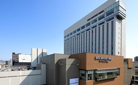 Das moderne Hotel Monterey Himeji präsentiert sich mit einer eleganten Fassade und klaren Linien unter einem strahlend blauen Himmel.
