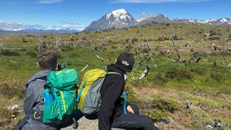 Zwei Kinder sitzen auf einem Felsen und blicken auf die beeindruckenden Torres del Paine in der Ferne.