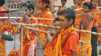 Eine Gruppe von Kindern in orangefarbener Kleidung, die mit Stöcken und Blumenkränzen an einem traditionellen Fest teilnehmen.