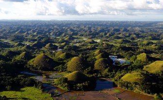 Die sanften, grünen Hügel der Chocolate Hills erstrecken sich über eine weite Landschaft, umgeben von üppiger Vegetation.