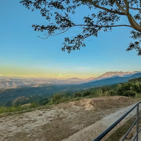 Ein atemberaubender Blick auf die sanften Hügel und Berge unter einem klaren blauen Himmel, umgeben von üppigem Grün.