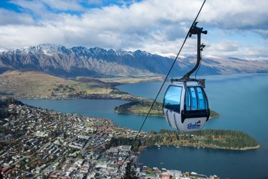 Eine Gondel schwebt über die malerische Landschaft von Queenstown, umgeben von majestätischen Bergen und glitzerndem Wasser.