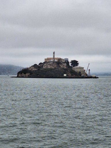 Die Insel Alcatraz ist von ruhigem Wasser umgeben, mit einem markanten Leuchtturm und historischen Gebäuden im Hintergrund.