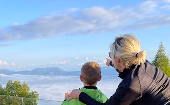 Eine Frau zeigt einem Jungen die majestätischen Himalaya-Berge, während sie über eine Wolkendecke blicken.