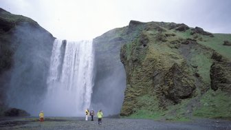 Ein beeindruckender Wasserfall stürzt in die Tiefe, während Besucher in bunten Regenjacken die Szenerie erkunden.