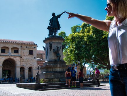 Eine Frau zeigt auf die Statue von Christoph Kolumbus im Parque Colón, umgeben von Besuchern und historischen Gebäuden.