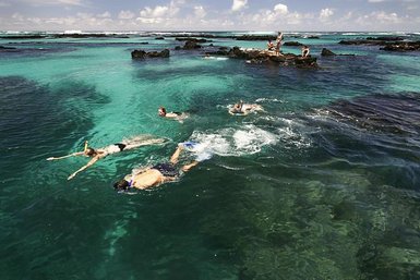 Im klaren, türkisfarbenen Wasser schwimmen mehrere Personen, während andere auf den Felsen entspannen und die Aussicht genießen.