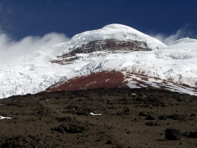 Der majestätische Vulkan Cotopaxi erhebt sich mit schneebedecktem Gipfel über die karge, vulkanische Landschaft.