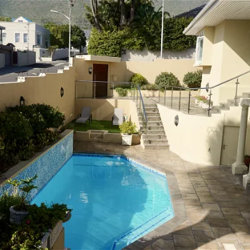 Ein einladender Pool in einem gepflegten Garten, umgeben von modernen Gebäuden und sanften Hügeln im Hintergrund.