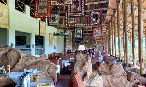 Ein einladendes Restaurant mit Holzdecke, dekoriert mit afrikanischen Wandteppichen und einem rustikalen Ambiente.