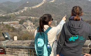 Zwei Frauen stehen auf der Chinesischen Mauer und zeigen auf die beeindruckende Landschaft der Berge im Hintergrund.