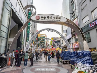 Eine belebte Straße während des Busan International Film Festivals, mit Menschen, die sich unter den geschwungenen Bögen bewegen.