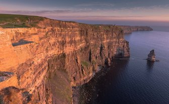 Die beeindruckenden Cliffs of Moher erheben sich majestätisch über den ruhigen Atlantik, beleuchtet von warmem Abendlicht.
