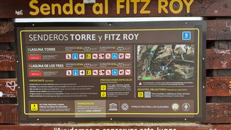 Ein Informationsschild weist auf die Wanderwege zu den Lagunen Torre und Fitz Roy in Patagonien hin, mit Distanzangaben.