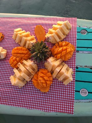 Auf einem karierten Tuch liegen kunstvoll geschnittene Ananas- und Mangostücke, umgeben von einer kleinen Ananas.