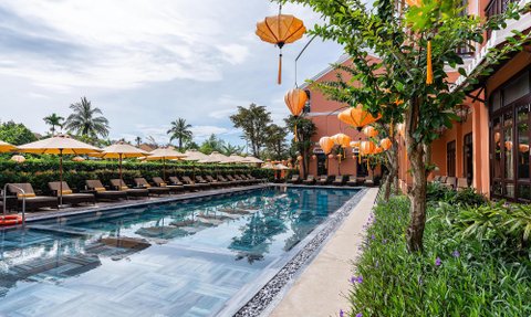 Ein eleganter Poolbereich mit Liegen und Sonnenschirmen, umgeben von üppigem Grün und leuchtenden Laternen.