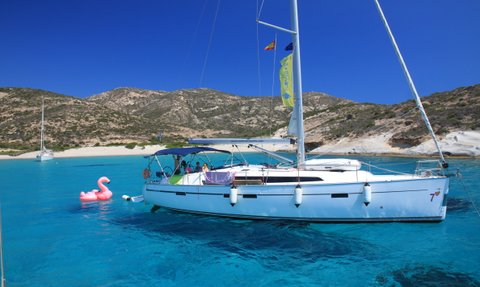 Ein Segelboot schaukelt sanft auf dem klaren, blauen Wasser, während ein pinker Flamingo-Schwimmring daneben schwimmt.